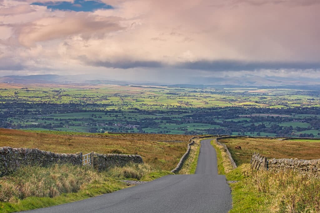 View looking down a Country Road near Staimore with the Eden Valley in the distance, Cumbria, England, UK.