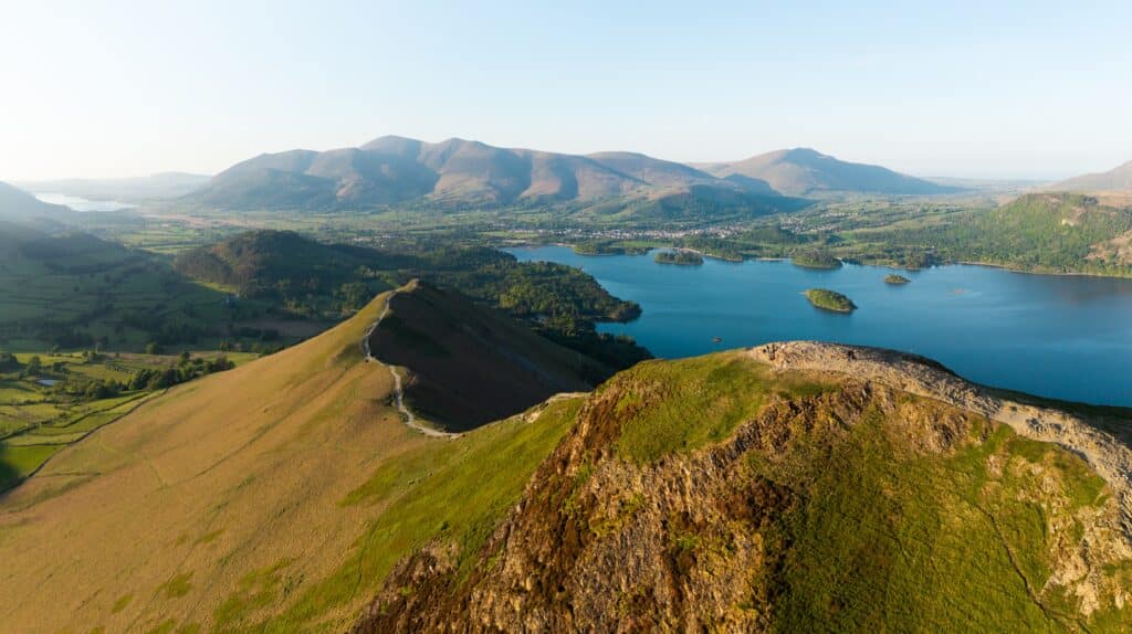 Aerial panorama landscape of the walking path along Catbells mountain ridge in the English Lake District National Park with Derwent Water lake and Keswick town below the Northern Fells on a sunny day