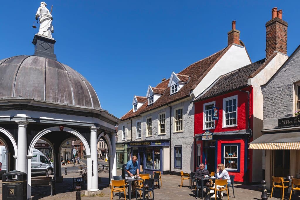 People relaxing at tables set up on the market square, by the Butter Cross, on a wonderfully sunny and warm day in the market town of Bungay.
