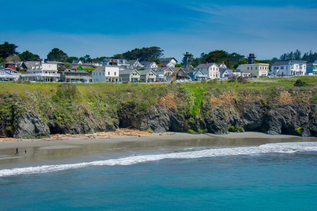 The seacoast village of Mendocino, California lines an ocean headland at low tide on a sunny spring afternoon.