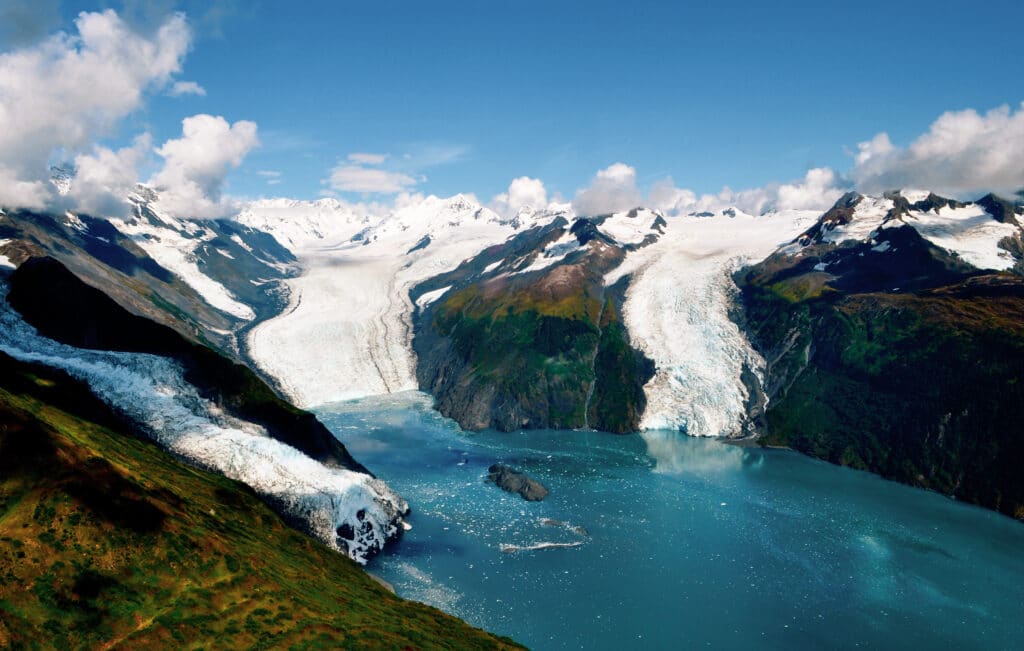 Aerial shot of three majestic glaciers calving into the beautiful azure blue waters of Prince William Sound, Kenai Peninsula. Icebergs float in the water below - Alaska