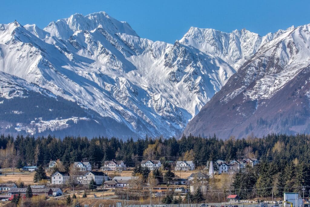 A small houses in rural field surrounded by trees and a snowy mountain in the background in Haines Alaska