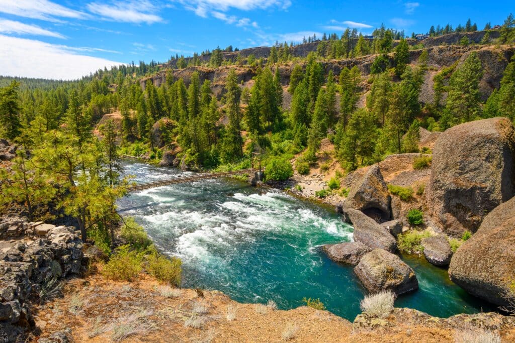 View from the highest point of Riverside State Park at the Bowl and Pitcher overlook showing the wooden suspension bridge across the Spokane River in Spokane Washington, USA.