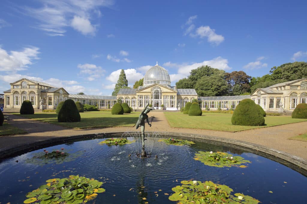 panorama of a large glass conservatory with a pond and fountain in the foreground