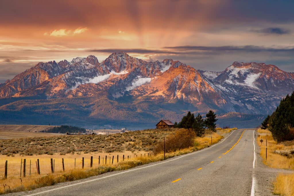 The Sawtooth mountains and a log cabin at sunrise and highway 75 leading to Stanley, Idaho.