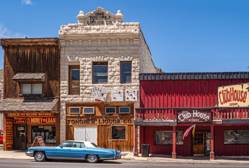 Tonopah, Nevada, US: Three historic buildings holding iconic businesses against blue sky. Offered are liquor, guns, gold, and more adjacent to Club House Saloon.