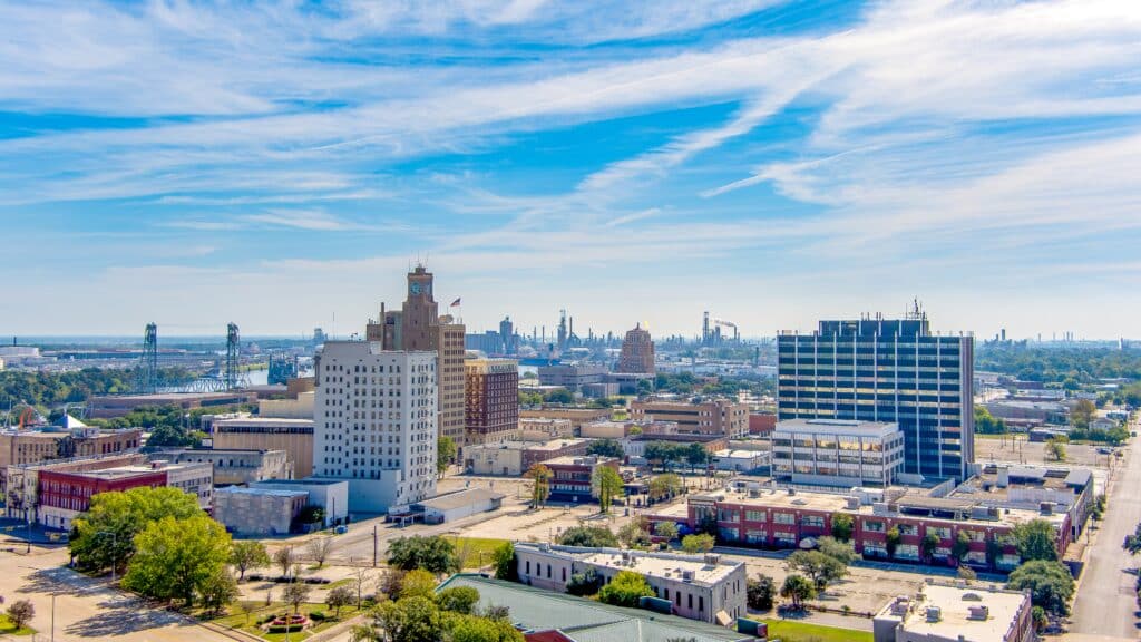 Aerial view of Beaumont Texas cityscape with modern and historic building, Fuel storage tanks, the Commercial Dock and Port and oil refineries in the background with a partly cloudy blue sky.