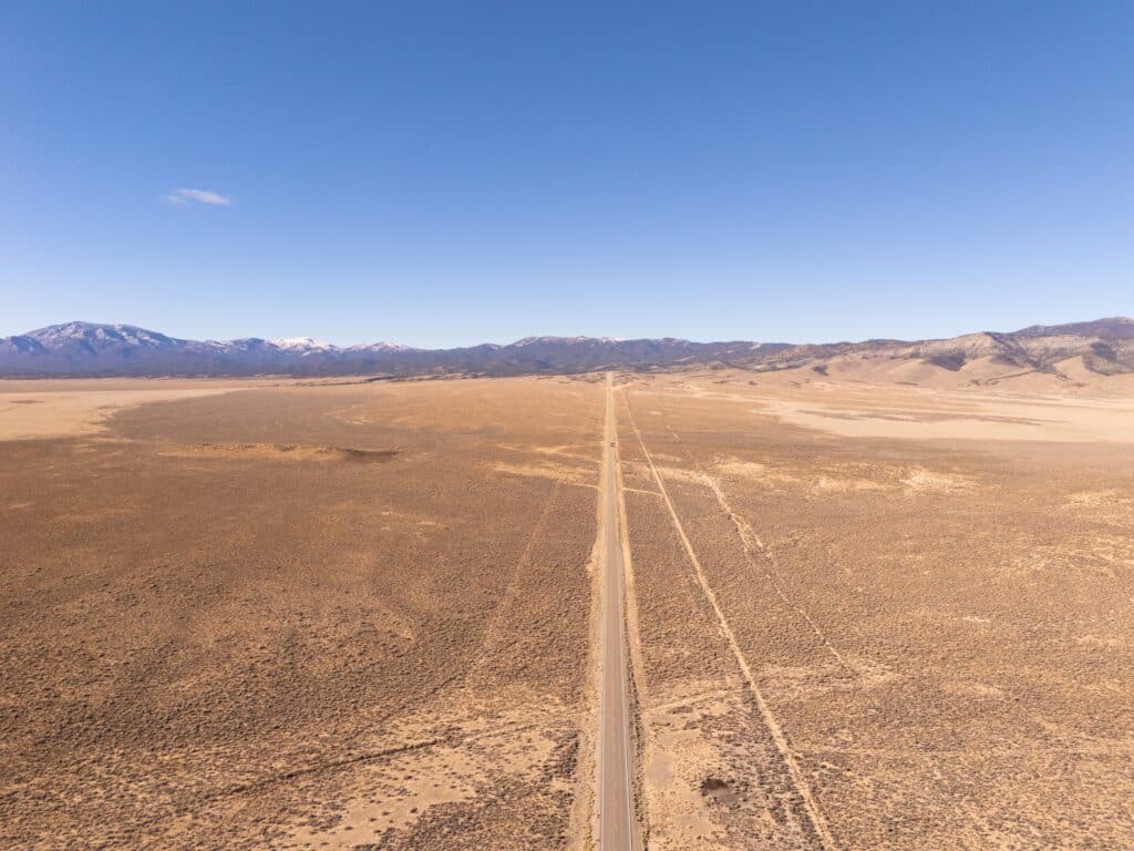 U.S. Route 50 in Nevada, the loneliest road in the USA, aerial view towards snowcapped mountains. Empty road and clear blue sky.