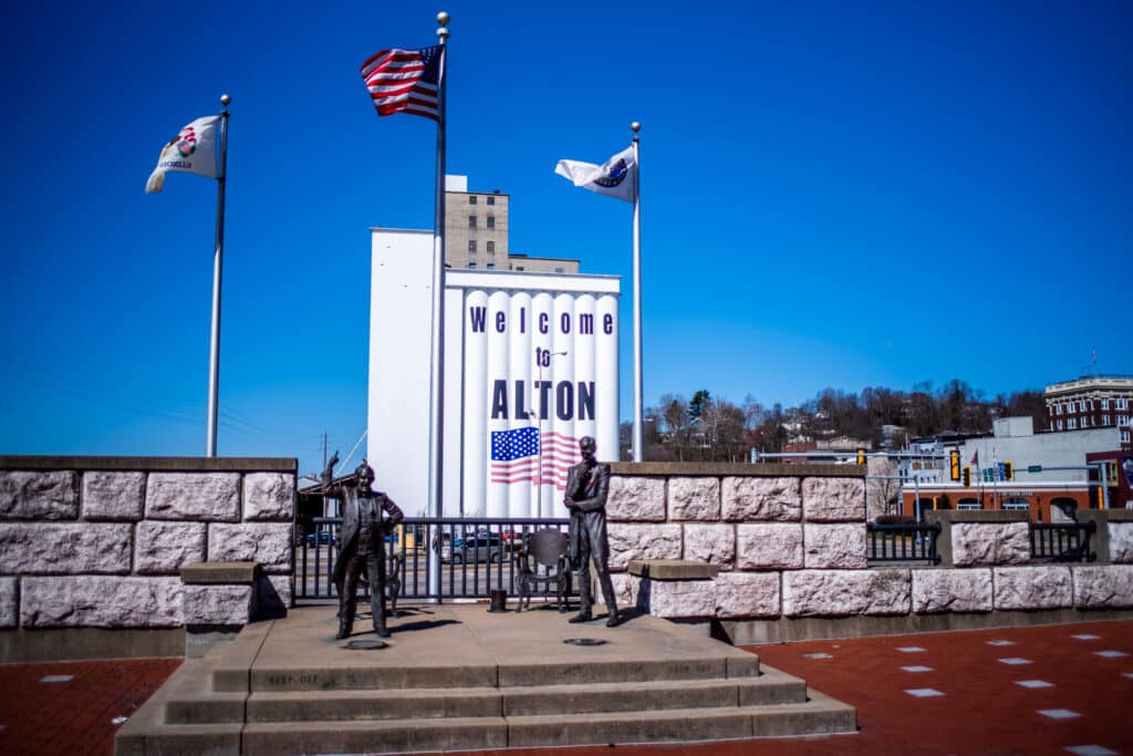 Alton, IL; Statues of Abraham Lincoln and Stephen Douglas stand in a park to commemorate the location of one of the Lincoln Douglas Debates with grain storage silos in background.