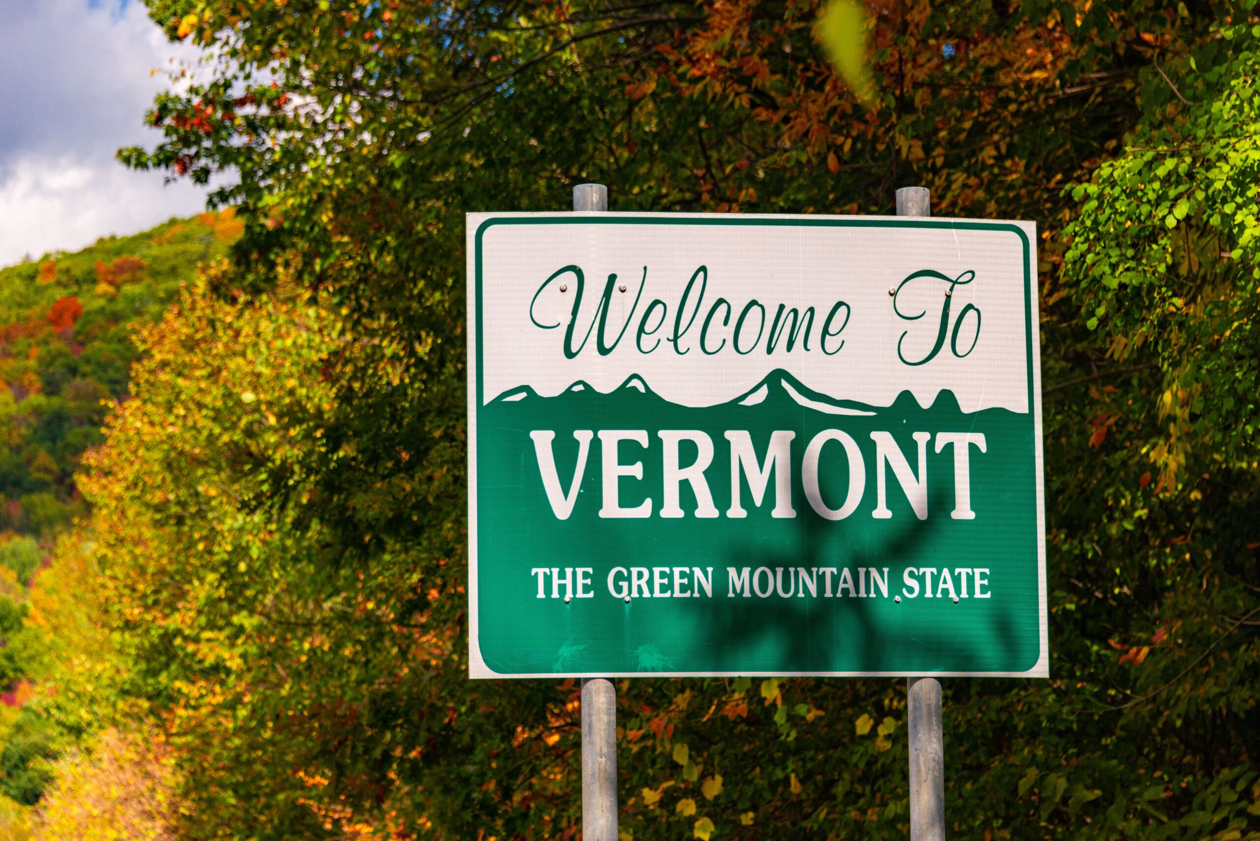 Welcome to Vermont state sign at road side with foliage in USA