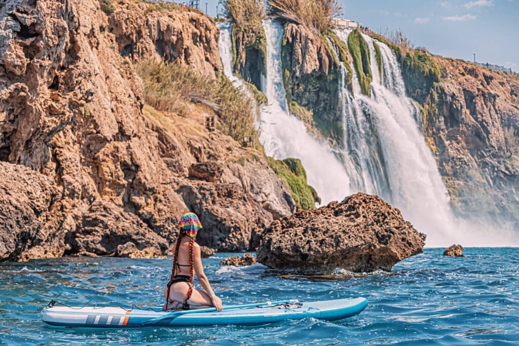 Happy girl on a SUP board near huge Duden waterfall in Antalya, Turkey. Summer watersports and recreation and adventure concept