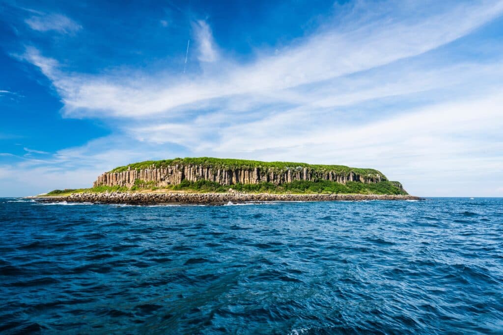 Beautiful view of Tongpan Island with a blue sky background in Penghu, Taiwan. The island is a basalt mesa landform with a shoreline of cliffs made of basalt columns.