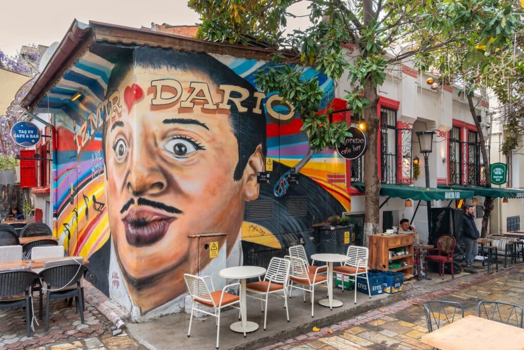 Izmir, Turkey: Street scene with large colorful mural of a face, Dario and Izmir text, outdoor seating area of Tas Ev Cafe and Bar and Moreno Bar, near Asansor