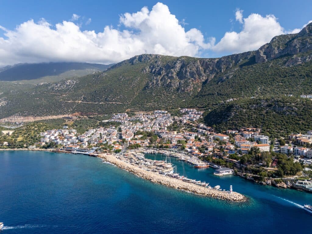 Aerial view of Kaş, with its colorful houses, a small harbor, turquoise waters, and surrounding rocky hills in Antalya, Turkey.