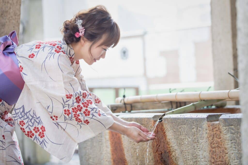 Woman in traditional kimono performing a purification ritual at a Japanese shrine water pavilion