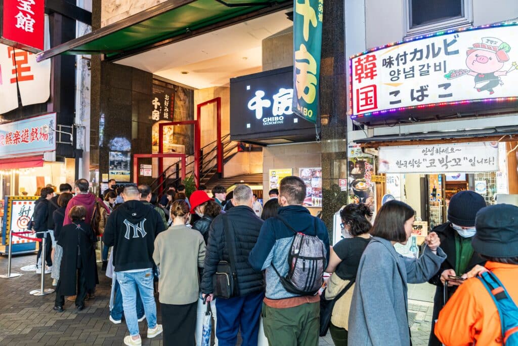 Visitors waiting in line outside a famous restaurant in Dotonbori