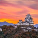 Himeji Castle glowing at sunset with surrounding mountains