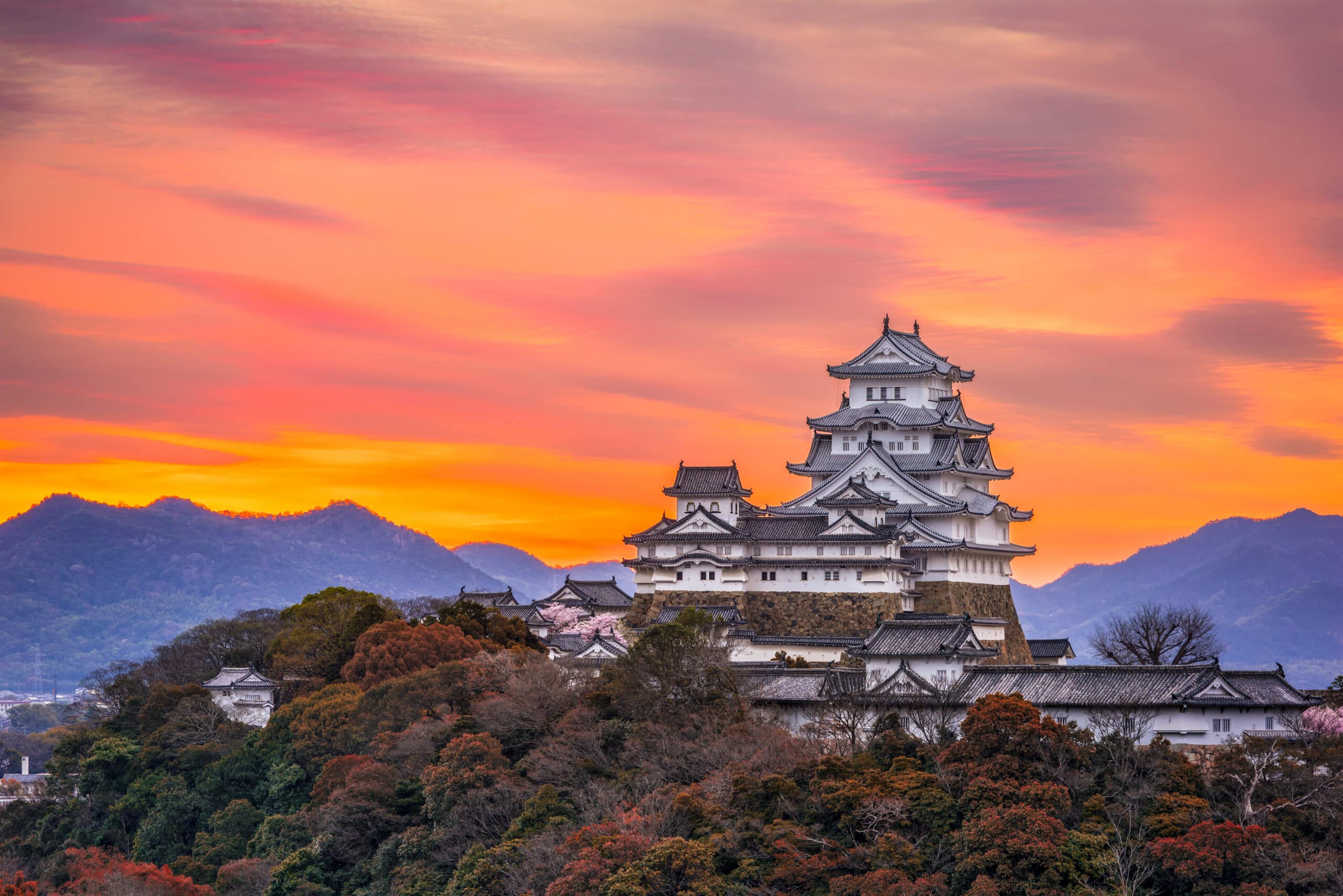 Himeji Castle glowing at sunset with surrounding mountains