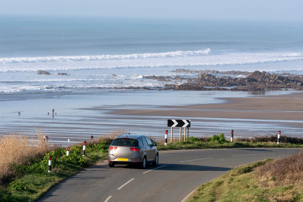 Car driving along a coastal road overlooking a beach in Cornwall