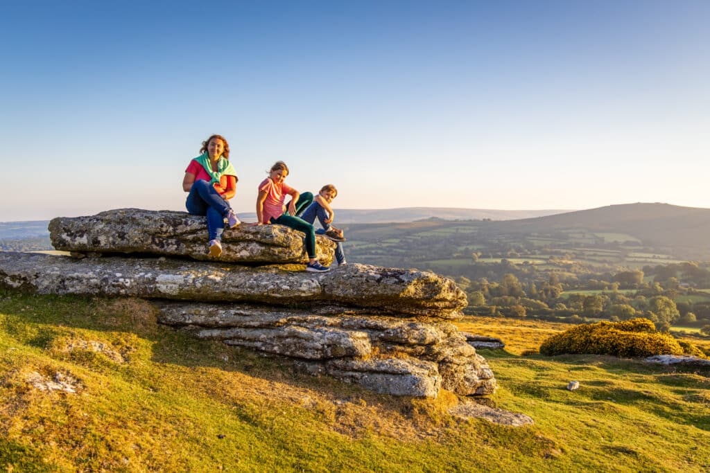 Family sitting on a granite outcrop overlooking the countryside in Dartmoor, Devon