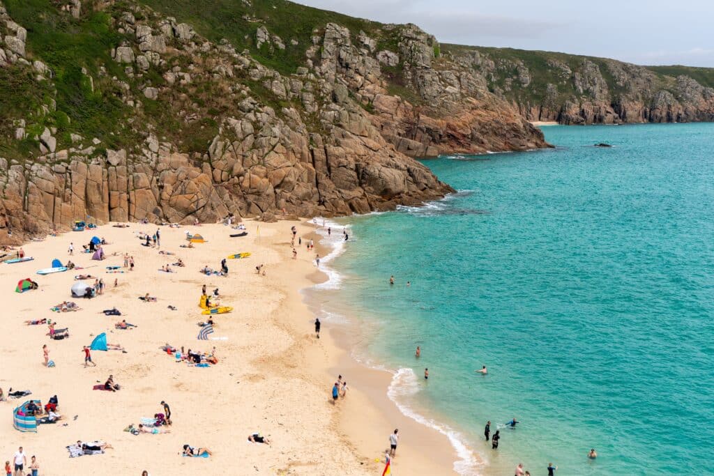 Porthcurno Beach surrounded by cliffs and turquoise water in Cornwall